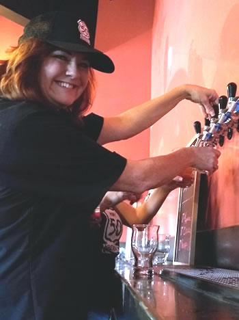 Woman in hat fills glass from a beer tap.