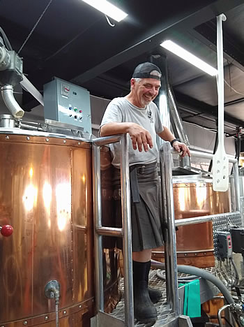 Brewer pauses to rest, copper vats of brew house.