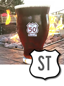 Dark Irish Stout in a Hwy 50 Brewery glass on edge of outdoor firepit.