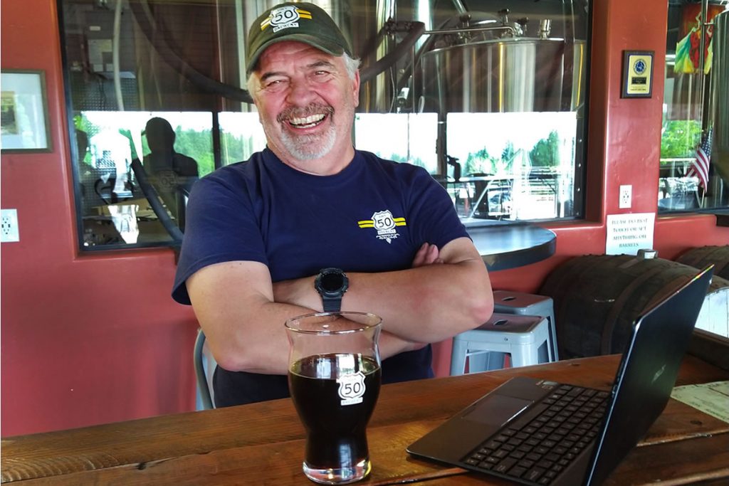 Hwy 50 Brewery Gary Ritz brewer, smiling, glass of porter on table.