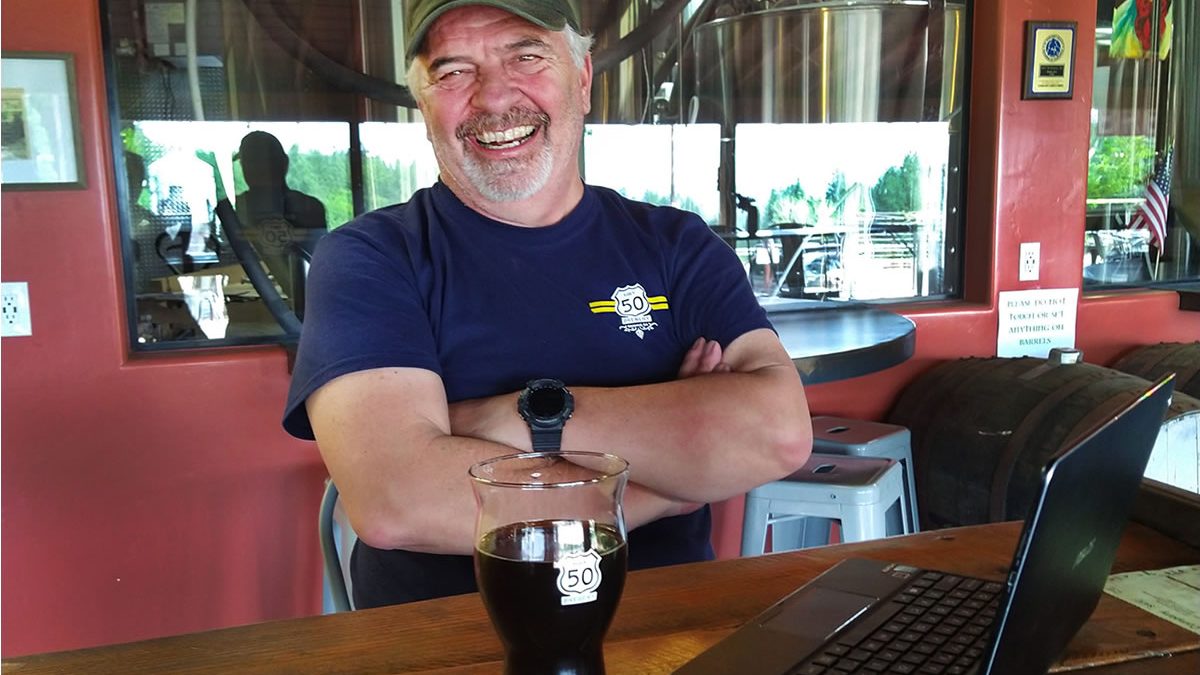 Hwy 50 Brewery Gary Ritz brewer, smiling, glass of porter on table.