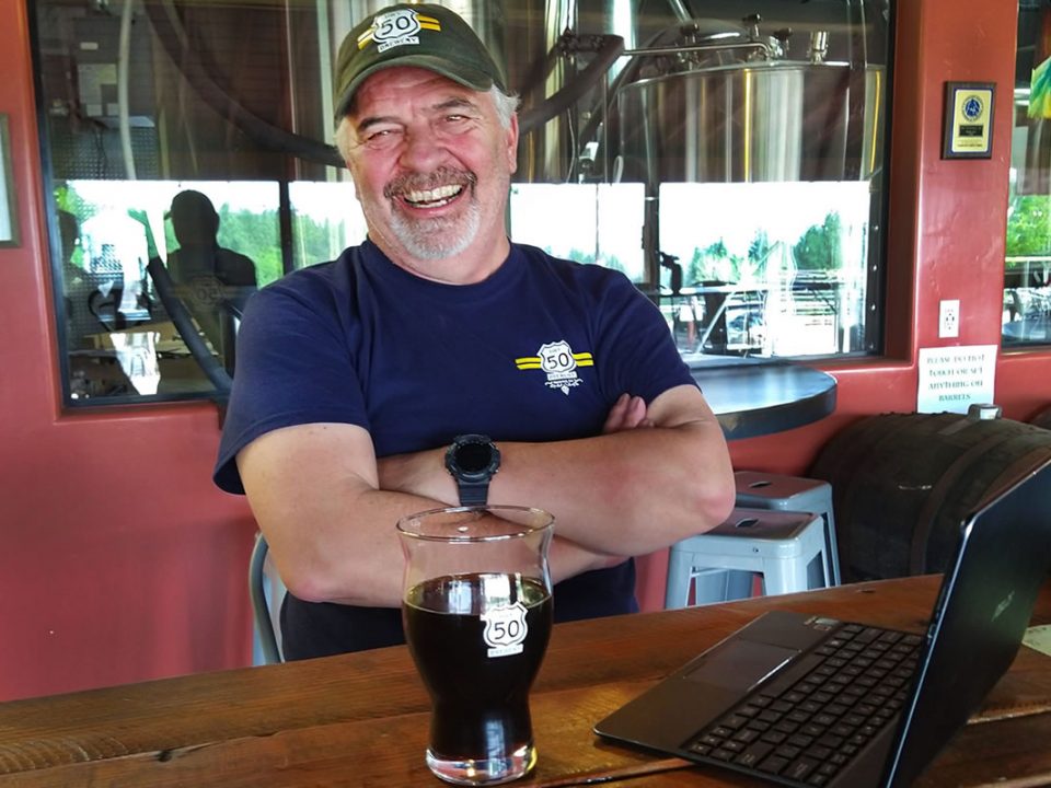 Hwy 50 Brewery Gary Ritz brewer, smiling, glass of porter on table.