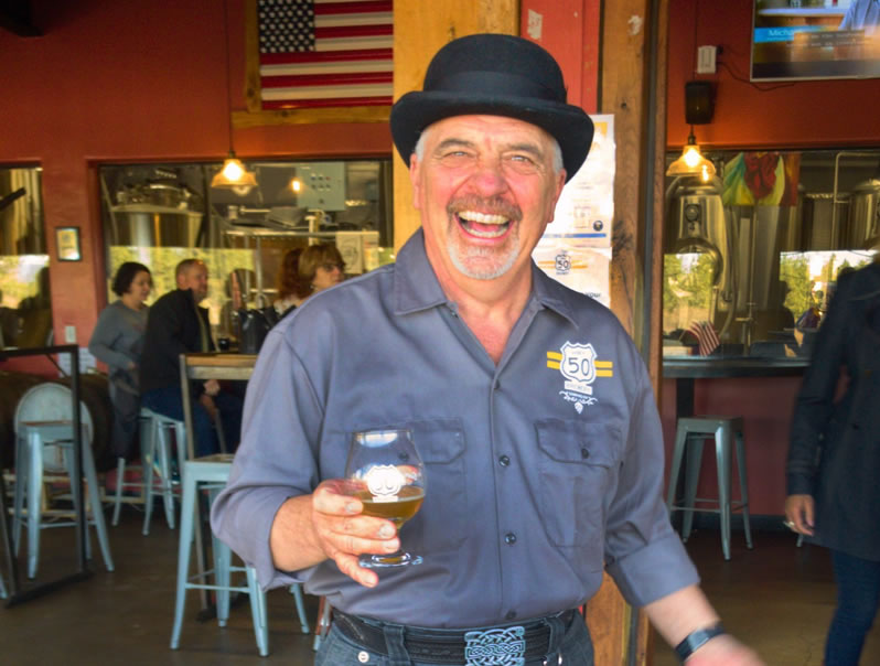 Brewer Gary Ritz, smiling in hat, with glass of beer in hand